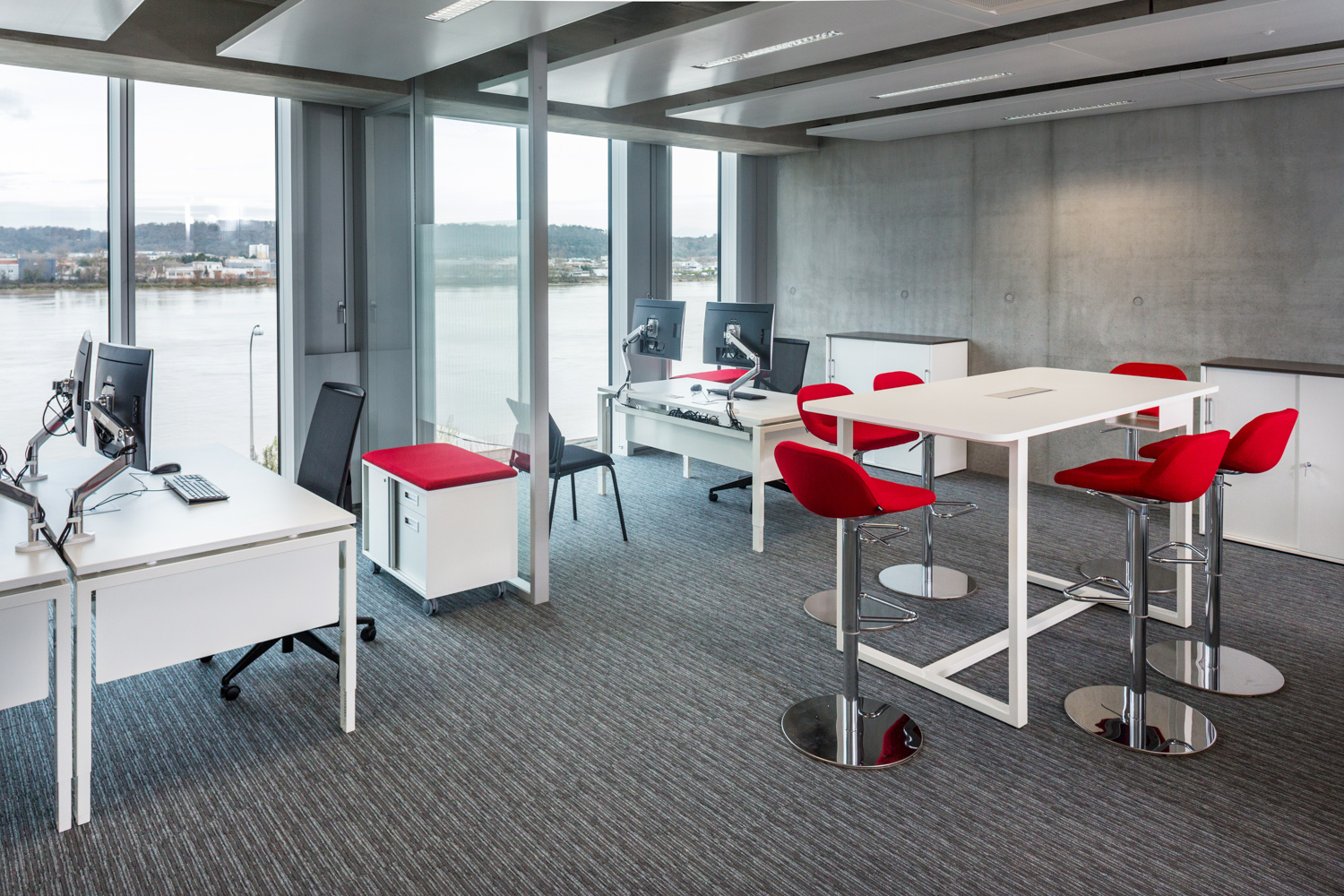 Mélange d'Open Space et d'espace de coworking, avec ses chaises hautes rouges et ses espaces de travail complet.