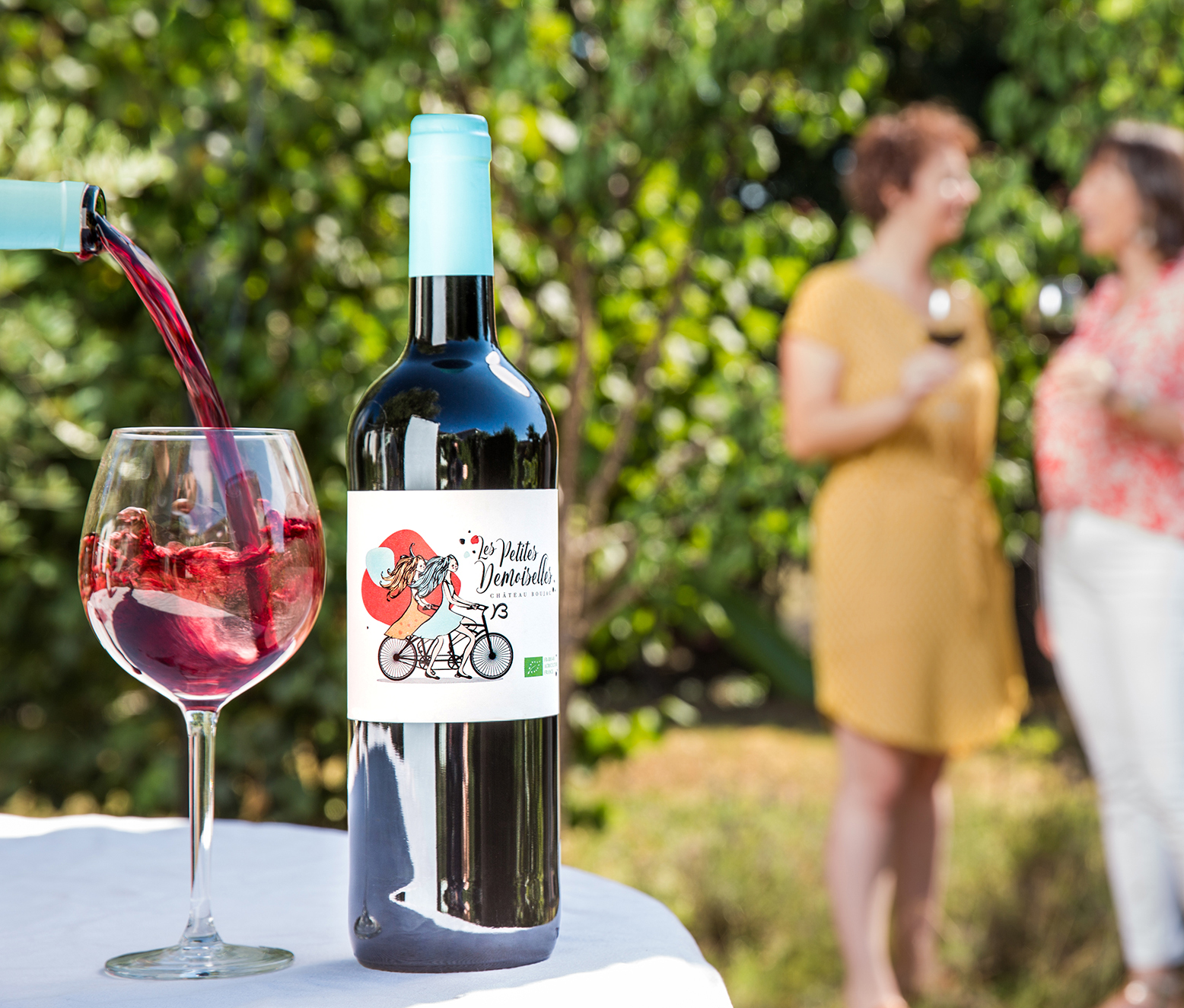 Verre de vin en train de se remplir avec le mouvement du vin dans le verre. Deux personnes discutent en arrière plan.