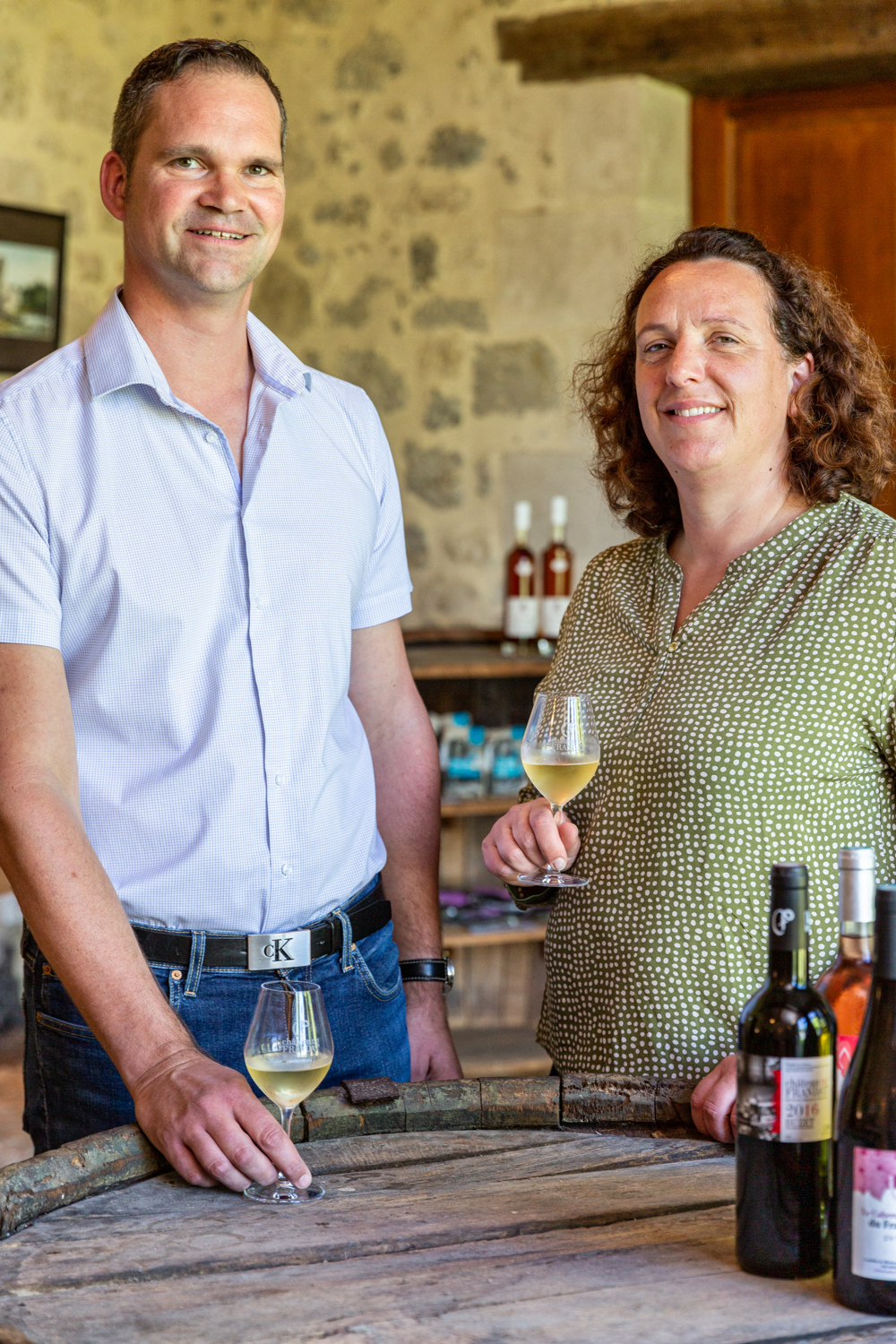 Photographie de deux vignerons posant devant leurs bouteilles de vin dans leur domaine